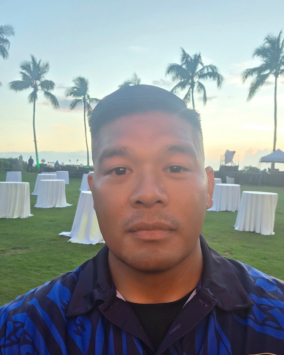 A Gold-Shield officer at an oceanfront event setup at golden hour, tables dressed behind him
