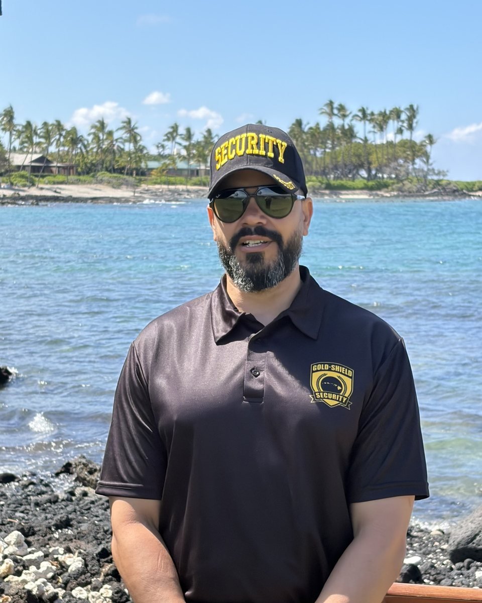 A Gold-Shield officer in a black uniform polo and cap standing on a shoreline post