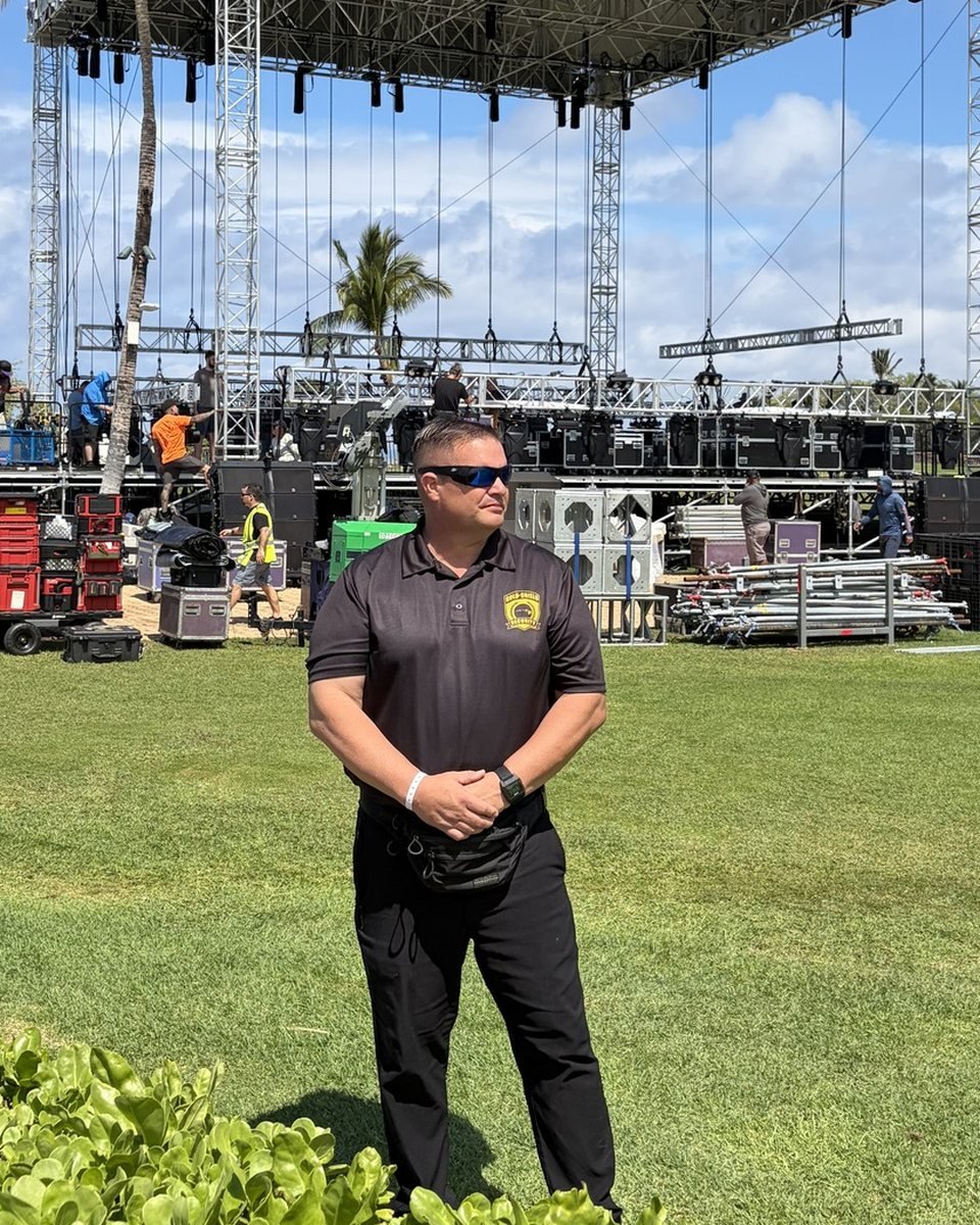 A Gold-Shield officer standing watch while a concert stage is built behind him